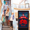 Shoppers in a mall looking at a digital floor sign advertising a sale
