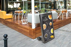 A portable digital sign advertises a restaurant menu next to the outdoor dining section.