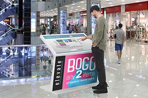 A man interacts with a digital wayfinding kiosk in a shopping mall.