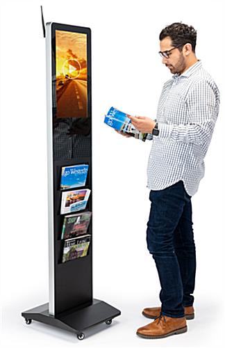 Man standing at a magazine rack digital display reading from a periodical