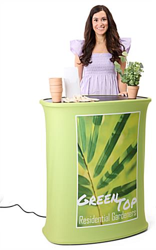 Woman standing behind pop up podium with custom graphics for a gardening company with plants and pots on top