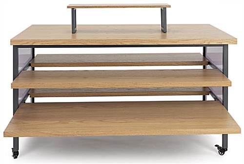Tiered display table with wheels and oak colored veneered MDF shelves