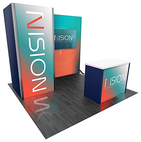 1016 10’ x 10’ Gravitee™ rental booth with small backlit backwall situated perpendicular to a larger backwall that is holding a monitor. In front of both backwalls is a backlit counter with locking storage and white countertop.
