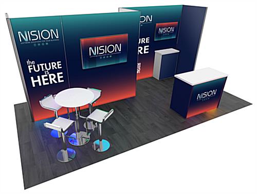 2013 20’ x 10’ Gravitee™ trade show booth rental seen from the left showing a backwall holding a monitor with a second backwall set further back to the right of it. A backlit podium sits in front of the recessed backwall in front of a smaller workstation. A high table with chairs is in front of the larger backwall